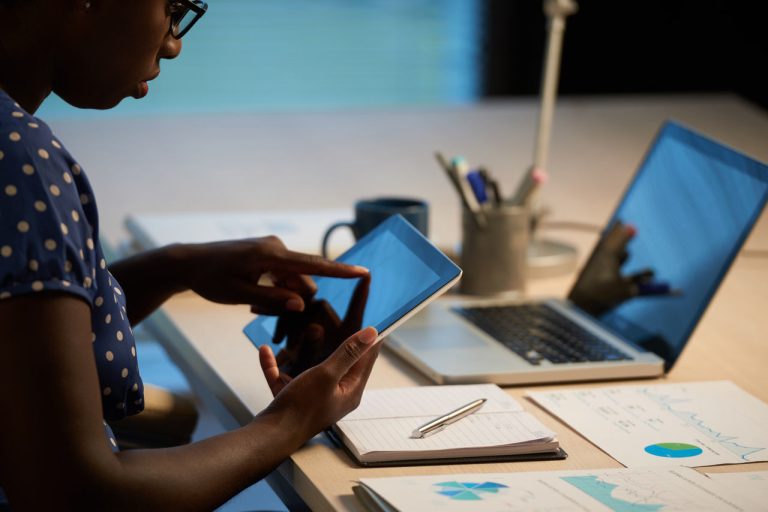 Growth hacking: mulher com tablet sentada em uma escrivaninha com materiais de escritório e laptop.