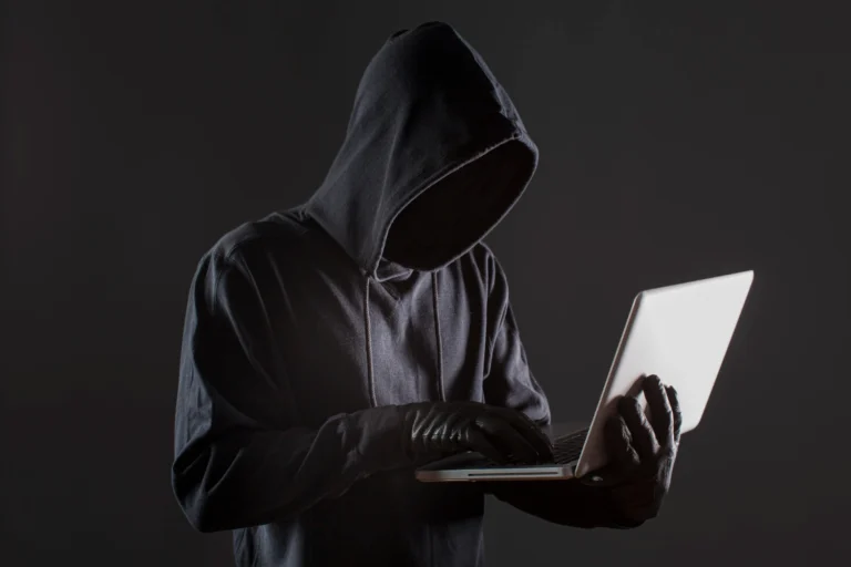 Golpes virtuais: pessoa vestida de moletom com gorro preto e luvas usando um laptop