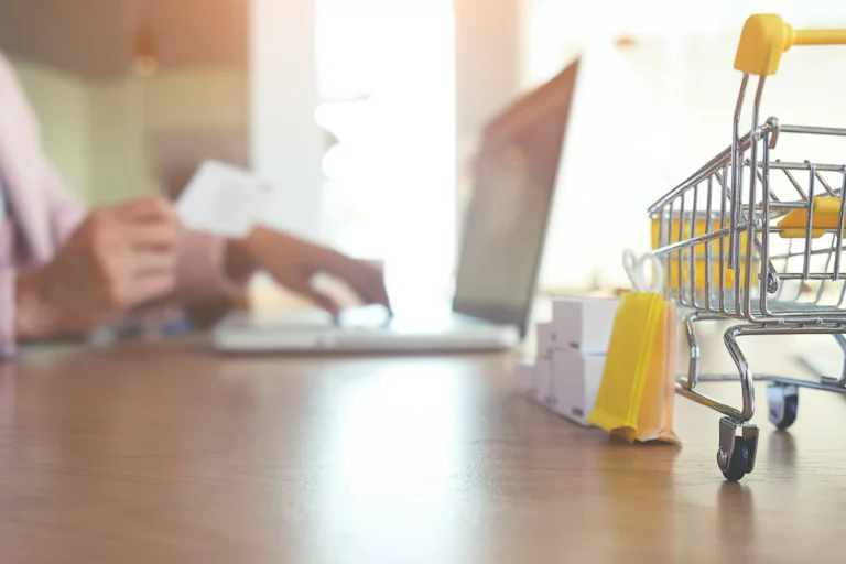 SEO para e-commerce: pessoa comprando pela internet com um laptop; carrinho de compras na mesa