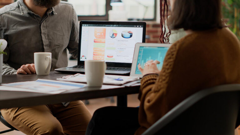 Dashboard de marketing B2B: pessoas trabalhando em um escritório, com notebooks abertos sobre a mesa de reunião exibindo gráficos e indicadores de desempenho.