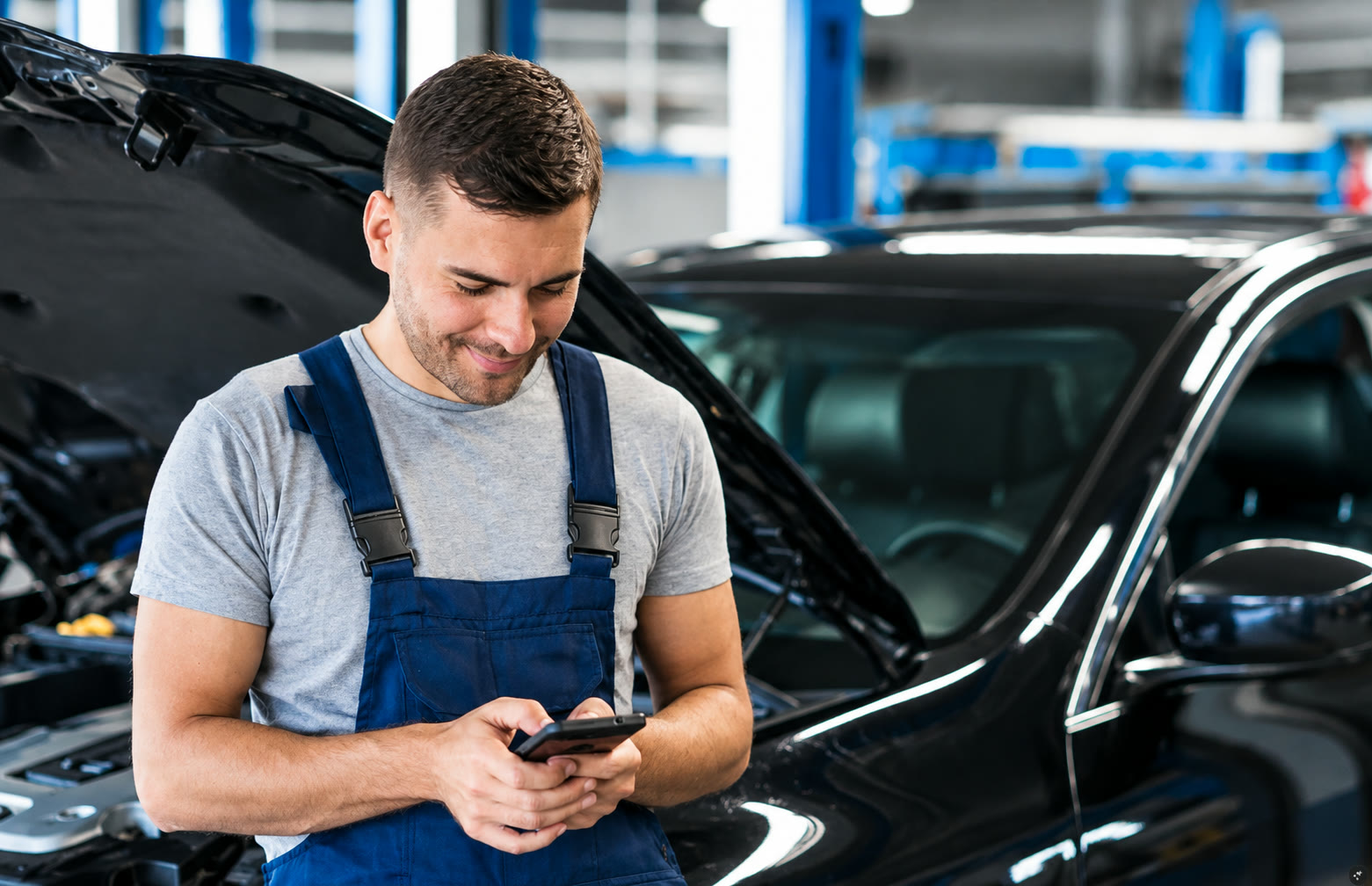 Marketing digital para indústria de autopeças: como estruturar demanda previsível no aftermarket 1 Marketing digital para indústria de autopeças: mecânico consultando o celular ao lado de um carro na oficina.