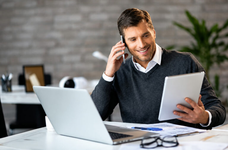 Outbound B2B na indústria: profissional de vendas ao telefone consultando o CRM no notebook, em escritório.